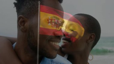 Sahilde kucaklaşan, İspanyol bayrak animasyonu yüzlerini kaplayan bir çift. Tatil, romantizm, seyahat, kutlama, çeşitlilik, neşe