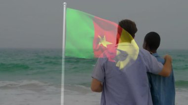 Kamerun bayrağıyla kumsalda kucaklaşan iki kişi anı paylaşıyor. Aşk, romantizm, vatanseverlik, günbatımı, birliktelik, kutlama