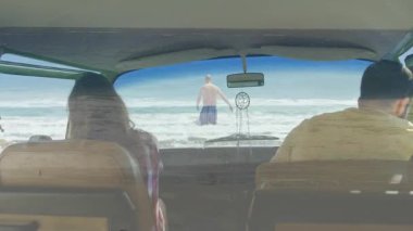 Okyanusa doğru yürürken, arabanın ön camından sarkan ve düş kapanı sallanan bir adam. Plaj, yaz, seyahat, macera, ufuk, keşif