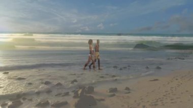 Kumsalda yürürken, insanlar arka planda okyanus dalgalarının ve animasyonların tadını çıkarıyorlar. Tatil, sahil şeridi, tatil, turizm, dinlenme.