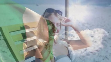 Sahilde dinlenen, İrlanda bayrağı animasyonuyla örtülü bir kadın, mutlu bir şekilde gülümsüyor. Tatil, rahatlama, yaz, seyahat, özgürlük, boş zaman