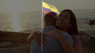 Günbatımı arka planında Kolombiya bayrağı animasyonu olan okyanus tarafından kucaklanan çift. Romantizm, kutlama, vatanseverlik, Karayipler, seyahat, eğlence
