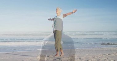 Kollarını neşeyle uzatan, yaşlı bir kadın sahilde, arkasında okyanus dalgaları olan. Deniz, rahatlık, rahatlık, rahatlama, yaz, tatil