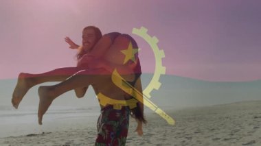 Kadını sahilde şakacı bir şekilde taşıyan, Angola bayrağının animasyonunu yapan adam. Tatil, çift, eğlence, romantik