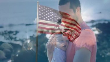 Amerikan bayrağı kaplanmış bebeği tutmak, okyanus arkasında dikilen adam. Vatanseverlik, yeni doğan, aile, deniz kenarı, kutlama, babalık