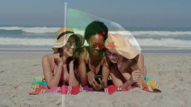 Kumsalda, güneş şapkalı kadınlar bayrak animasyonlarıyla akıllı telefonlara bakıyor. Tatil, turizm, rahatlama, yaz, tropik, moda