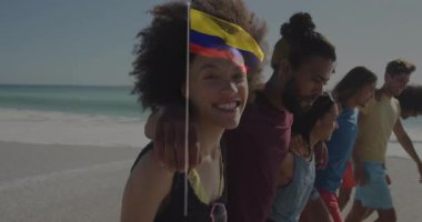 Kolombiya bayrağı animasyon örtüsüyle sahilde yürüyen bir grup arkadaş. Tatil, seyahat, Kolombiya kültürü, gün batımı, kutlama, açık hava