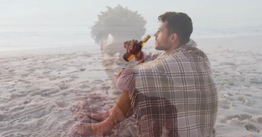 Kumsalda oturan, battaniyeye sarılmış bir adam, başka bir insanın animasyon örtüsü. Rahatlama, rahatlama, tatil, okyanus, rahatlama, rahatlama