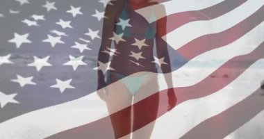 Sahilde, arka planda Amerikan bayrağı animasyonu olan mayolu bir kadın. Tatil, vatanseverlik, özgürlük, yaz, okyanus, rahatlama