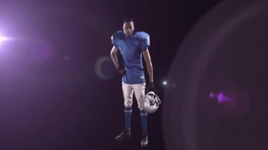 Kask tutan, mavi üniformalı Amerikan futbolcu spot ışıkları altında duruyor. Spor, atlet, yarışma, takım çalışması, kararlılık, güç