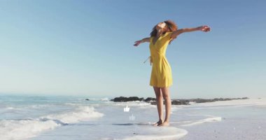 Güneşli sahilde, sarı elbiseli bir kadın okyanus esintisini hissediyordu. Tatil, rahatlama, tropikal, kıyı, ilham, yaratıcılık