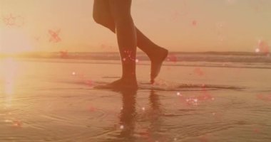 Sahilde yalınayak yürüyen, gün batımında parlayan kırmızı parçacıklarla çevrili biri. Huzur, meditasyon, rahatlama, canlılık, huzur.