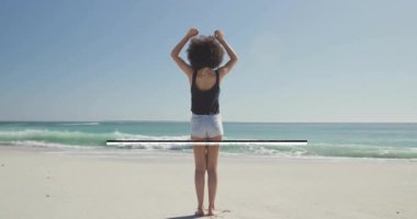 Sahilde duran, kollarını kaldıran, okyanus dalgalarına bakan, özgür hisseden biri. Özgürlük, huzur, sükunet, sahil şeridi, rahatlama, meditasyon.