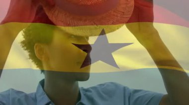 Hasır şapkayı Gana bayrağıyla kaplamak, dışarıda ayakta durup gülümseyen biri. Vatanseverlik, başlık, ulusal bayrak, yaz, geleneksel, neşeli