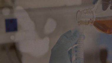 Mezuniyet silindirine sıvı dökülüyor, eldivenli eller laboratuvar ortamında çalışıyor. Bilim, deney, kimya, araştırma, ekipman, güvenlik
