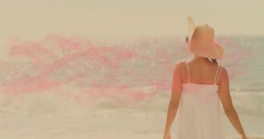 Beyaz elbiseli ve şapkalı bir kadın pembe dalga animasyonuyla plajın tadını çıkarıyor. Tatil, yaz, rahatlama, moda, dinginlik, kıyı