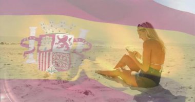 Sahilde oturan, arka planda İspanyol bayrağı olan bir kadın. Yaz, dinlenme, tatil, seyahat, turizm, sahil