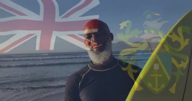 Union Jack 'le sörf tahtası tutmak, sahilde hareketli gülümseyen adam. Sörf, tatil, yaz, dalgalar, okyanus, macera