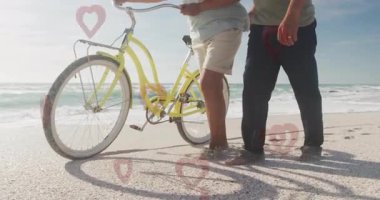 Sahilde yürüyen, bisikletli yaşlı bir çift, sahnede kalp animasyonu. Yaşlılar, romantizm, bisiklet, günbatımı, tatil, aşk