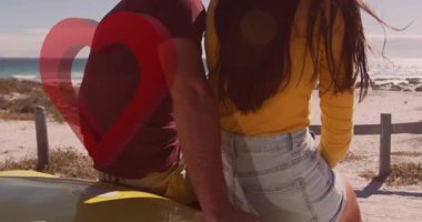 Sahilde oturan, kalp animasyonuyla romantik anın tadını çıkaran bir çift. Aşk, aşk, tatil, gün batımı, manzara