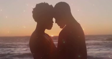 Gün batımında okyanus kenarında parıldayan ışıkları olan siluetli bir çift. Romantizm, alacakaranlık, dinginlik, beraberlik, ışık, şefkat