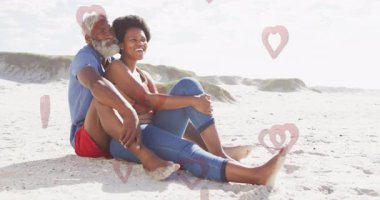 Sahilde oturan yaşlı bir çift kalp animasyonlarıyla sahneyi örtüyor. Yaşlılar, romantizm, aşk, tatil, seyahat, ilişki