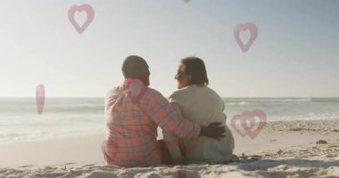 Sahilde, birlikte oturan bir çift kalp animasyonu sahnesiyle örtüşüyor. Aşk, aşk, deniz kenarı, tatil, seyahat, tatil