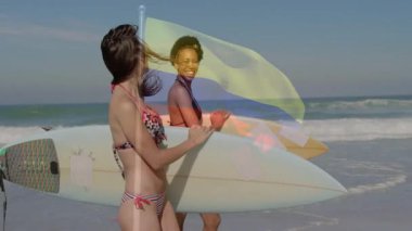 Sahilde sörf tahtası olan iki kadın, sahne üstünde Kolombiya bayrağı animasyonu. Sörf, okyanus, arkadaşlar, macera, seyahat, yaşam tarzı