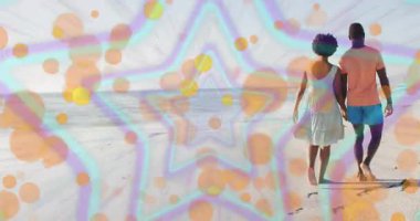 Renkli yıldız ve çember şeklinde animasyon örtüsüyle kumsalda yürüyen çift. Romantik, tatil, gün batımı