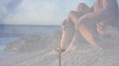 Okyanus kıyısındaki kayalarda oturan, animasyonda haç sembolü olan kadın. Maneviyat, dinginlik, meditasyon, doğa, rahatlama, kıyı