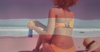 Güneş kremi tutuyor, güneşli sahilde dalgalı turuncu mayo giymiş bir kadın. Yaz, yüzme, tatil, güneşlenme, seyahat, deniz kenarı