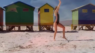 Kumsalda, renkli sahil kulübelerinin yanında takla atan bir çocuk, animasyonun tadını çıkarıyor. Yaz, çocuklar, deniz kenarı, tatil, deniz kenarı aktiviteleri, eğlence