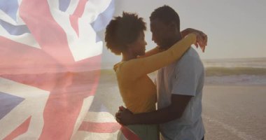 Sahilde kucaklaşan, arka planda İngiliz bayrağı animasyonu olan çift. Romantizm, vatanseverlik, deniz kenarı, bağlılık, birlik, aşk