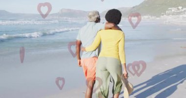 Kumsalda yürüyen, romantik ortamda kalp animasyonlarıyla çevrili bir çift. Romantizm, aşk, günbatımı, birliktelik, tatil