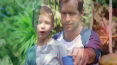 Bahçede, baba çocuğun güneşli gökyüzünün altında mavi bardaktan su içmesine yardım ediyor. Ebeveynlik, aile, bağ, doğa, susuzluk, yardım