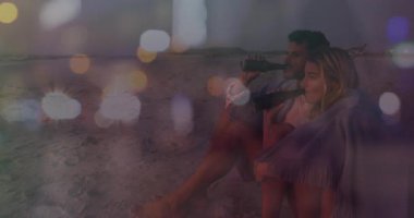 Alacakaranlıkta sahilde oturan çift renkli ışık animasyonunun tadını çıkarıyor. Günbatımı, romantizm, tatil, sahil, rahatlama, sükunet