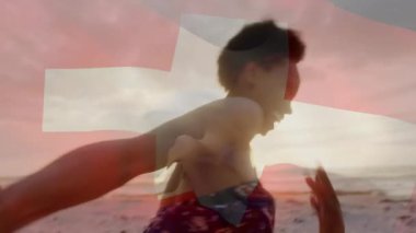 Sahilde el ele tutuşan İsviçre bayrak animasyonu arka planda güneş ışığı ile örtüşüyor. Romantizm, tatil, aşk, seyahat, macera, vatanseverlik