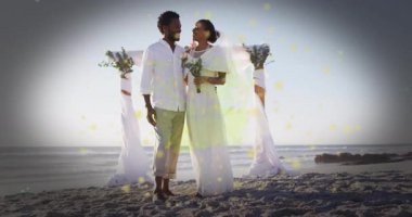 Kumsalda, parıldayan ışık efektleri ve ellerinde çiçeklerle çevrili bir çift. Romantik, günbatımı, aşk, tatil, kutlama, doğa