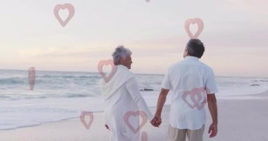 Sahilde yürüyorlar, yaşlı bir çift kalp animasyonuyla el ele tutuşuyorlar. Romantizm, günbatımı, aşk, altın saat, sahil şeridi, birliktelik