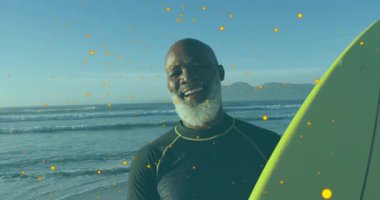 Sahilde, etrafı ışıldayan animasyon parçacıklarıyla çevrili sörf tahtası olan bir adam gülümsüyor. Sörf, okyanus, dijital, eğlence, tatil, açık hava