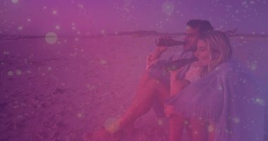 Sahilde oturmuş, çift pembe kaplamalı animasyon seyrediyor. Tatil, romantizm, eğlence, rahatlama, okyanus, deniz