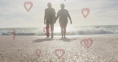 Sahilde yürüyorlar, yaşlı bir çift kalp şeklinde el ele tutuşuyorlar. Romantizm, aşk, yaşlılar, birliktelik, bağ, gezinti