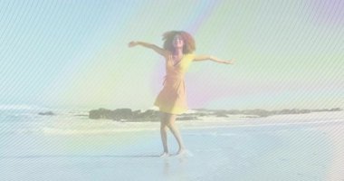 Neşeli bir şekilde dönen, kumsalda gökkuşağı animasyonlu sarı elbiseli kadın. Yaz, renkli, tasasız, mutluluk, dans, okyanus