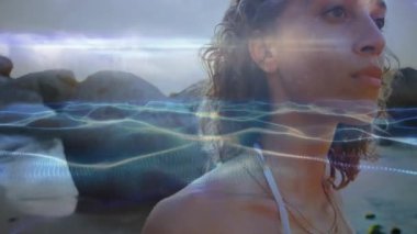 Sahilde, yüzünü kaplayan soyut ışık dalgalarının animasyonuyla bir kadın. Doğa, rahatlama, sükunet, güneş ışığı, yaz, okyanus.