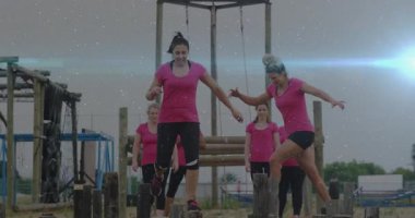 Açık hava engelli parkurunda dengede duran pembe tişörtlü kadınlar kararlılık gösteriyor. Takım çalışması, macera, güç, fitness, meydan okuma, egzersiz