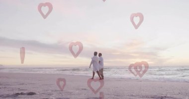 Sahilde yürüyen, kalp şeklinde animasyonu olan sakin okyanus manzaralı bir çift. Aşk, gün batımı, tatil, dinginlik, sükunet, kumlu