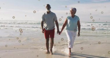 Baloncuklu animasyon örtüsüyle kumsalda el ele yürüyen yaşlı bir çift. Emeklilik, gün batımı, romantizm, boş zaman, altın yıllar, sükunet