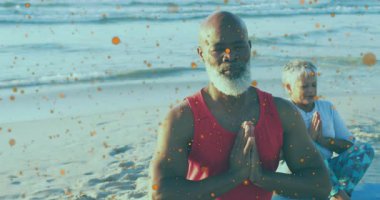 Yaşlı çift plajda turuncu parçacıklar eşliğinde yoga yapıyor. Meditasyon, sağlık, rahatlama, okyanus, günbatımı, fitness
