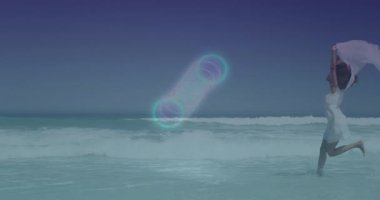 Sahilde koşan, renkli ışık desenli bir kadın gökyüzünde animasyon yaratıyor. Spor, sağlık, teknoloji, yaratıcılık, günbatımı