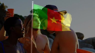 Kumsalda güneşli bir günde dinlenen insanların üzerinde kamerun bayrağı dalgalanması. Rahatlama, tatil, vatanseverlik, seyahat, turizm, deniz kenarı